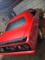 Red Plymouth Cuda parked in a garage, features clean exterior and racing stripe