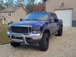 Blue 2004 Ford F350 King Ranch 4x4 with aftermarket wheels and power features parked at a house.